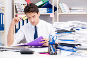 Blog post - worker frustrated by all of the papers on his desk