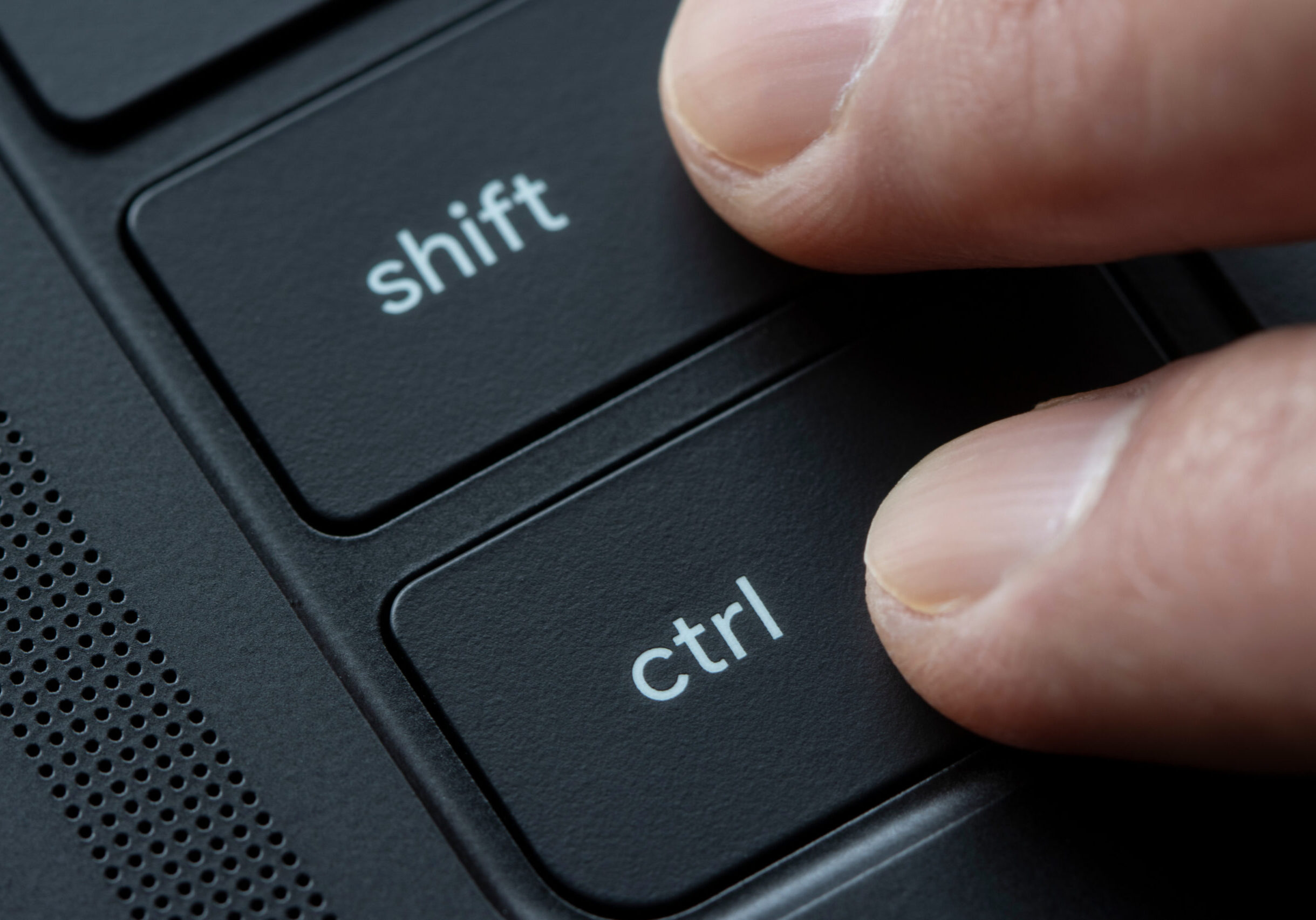 Fingers holding down Shift and Ctrl keys together on a black laptop computer.